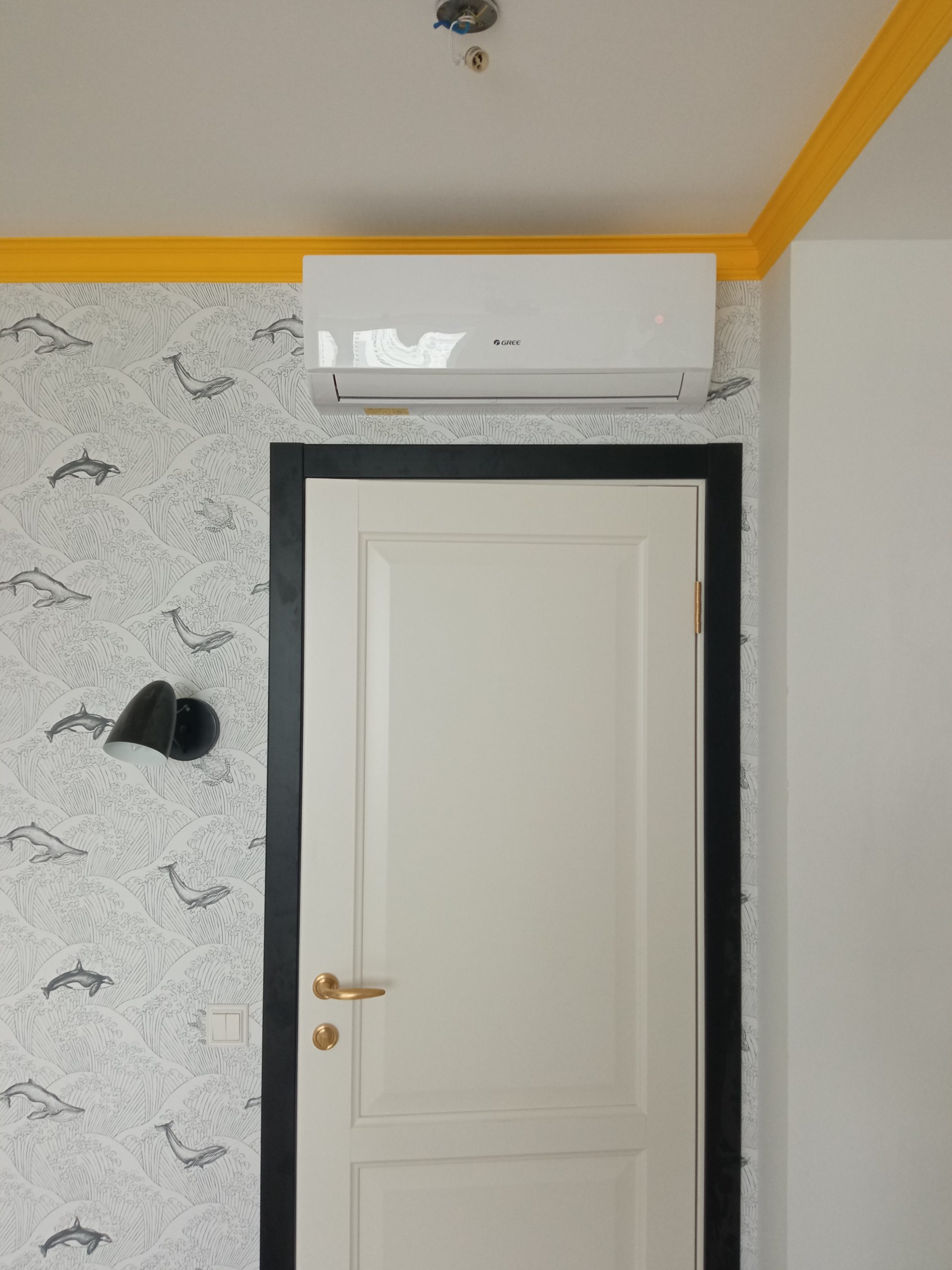 Белый кондиционер Gree над дверью на черно белой стене с желтым плинтусом